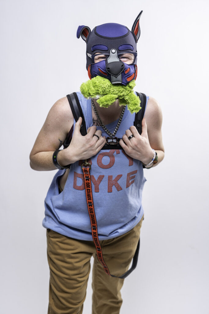 Pup Ace laughing as they hold a stuffed green plush toy in their mouth.