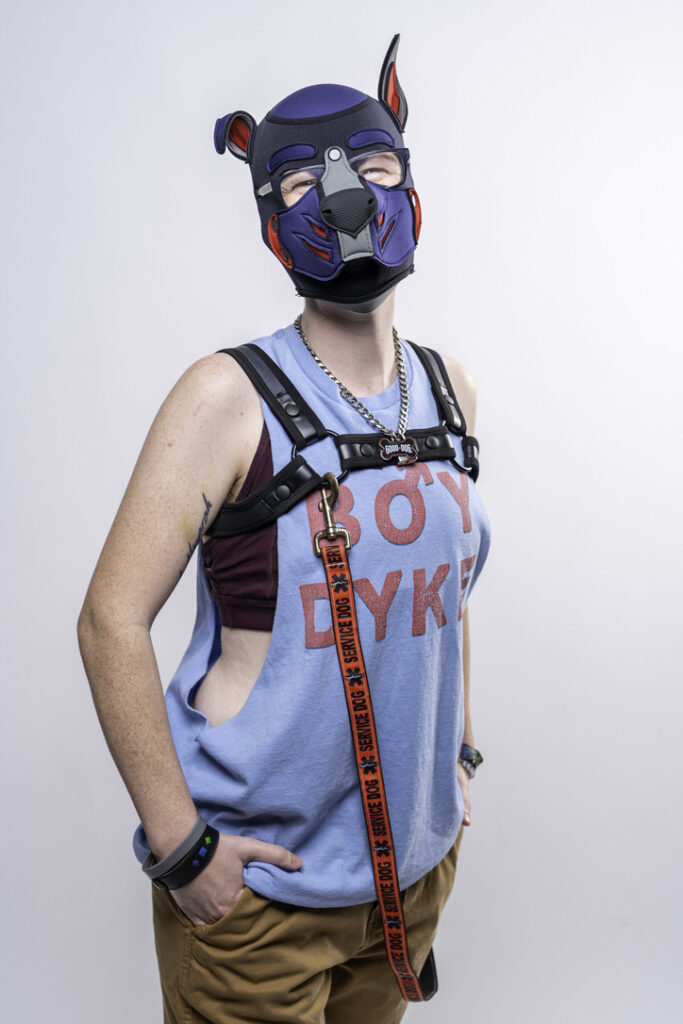 Pup Ace standing and smiling at the camera wearing a shirt that says 'Boy Dyke'